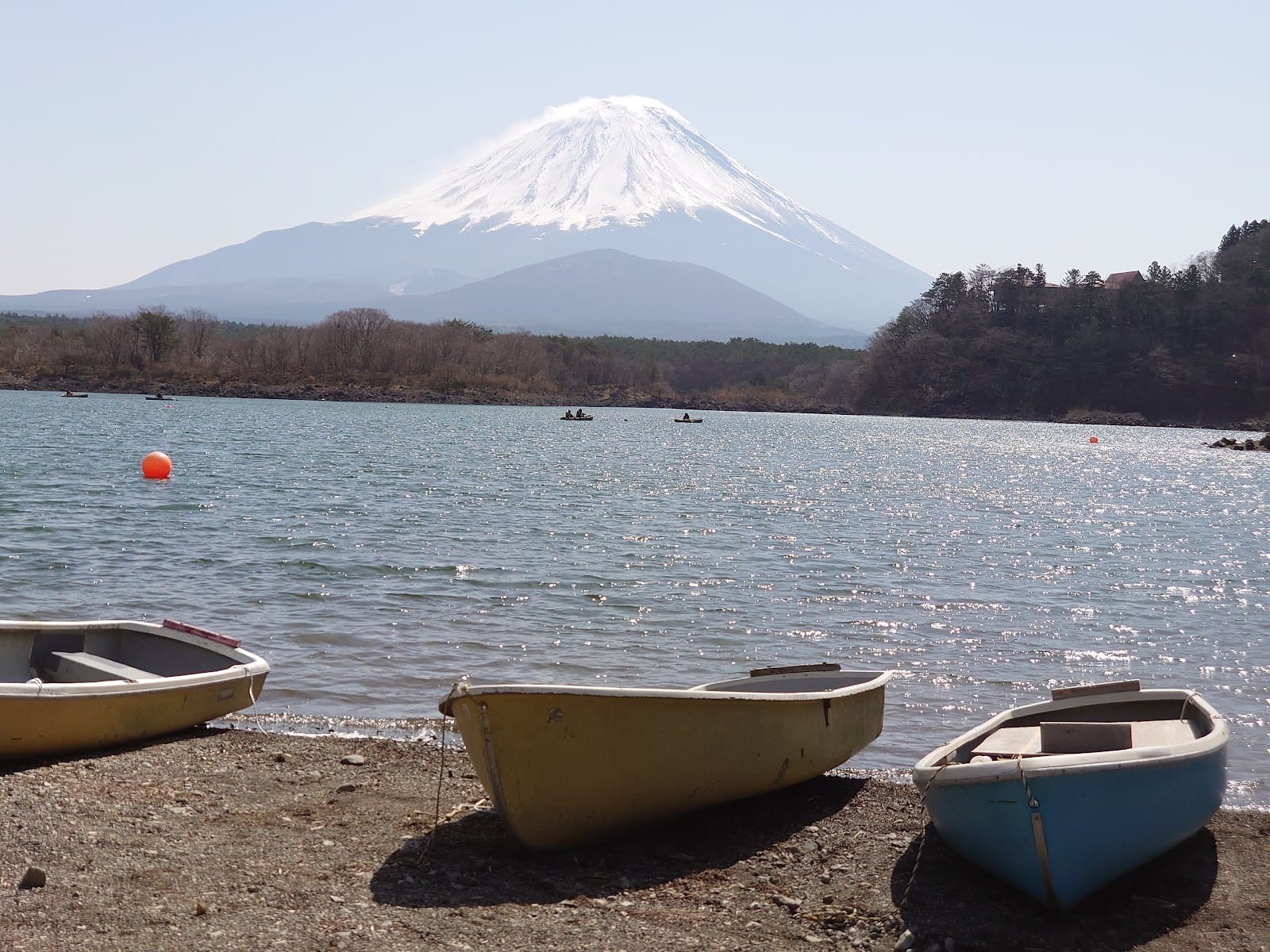 Snow-capped Mt. Fuji above Lake Kawaguchi with small boats drawn up on the shore.