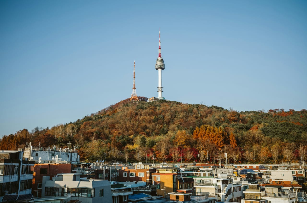 N Seoul Tower rises above a wooded hill and rooftops in Seoul.