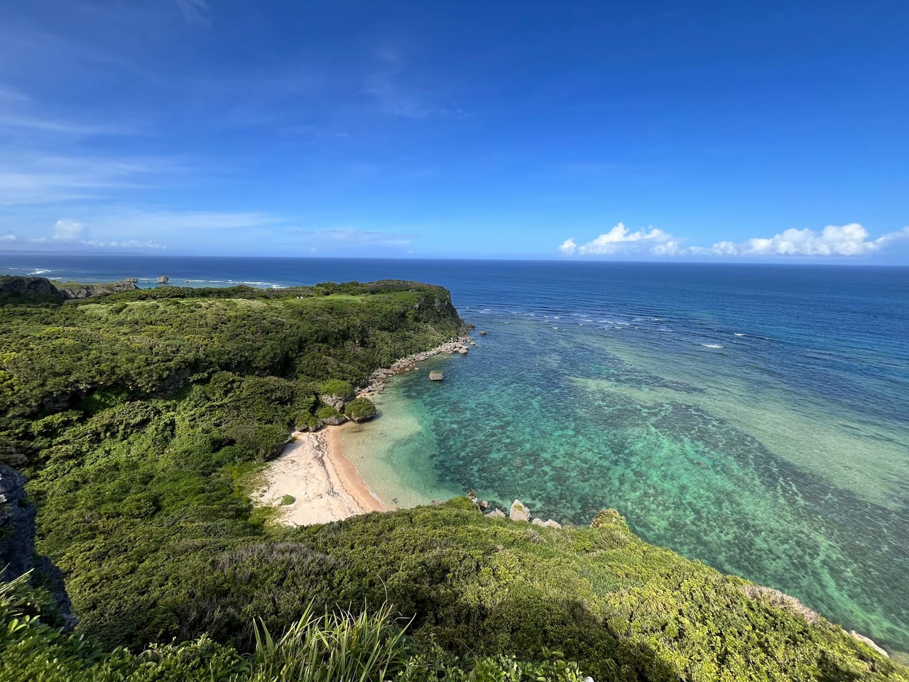 A forested rocky coastline with a small sandy cove and clear blue water.