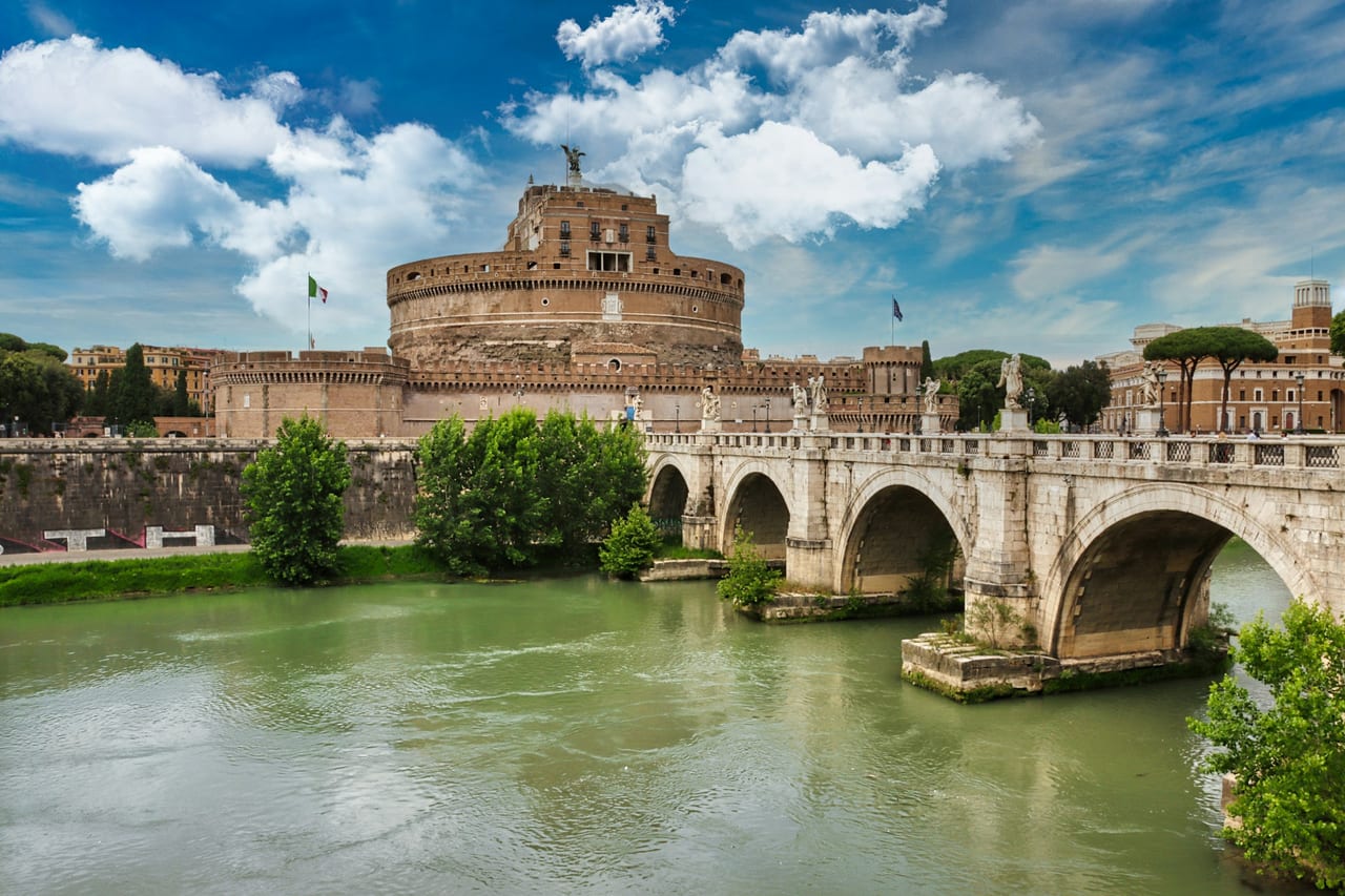 The round fortress of Castel Sant'Angelo rises across the Tiber beyond its statue-lined bridge.