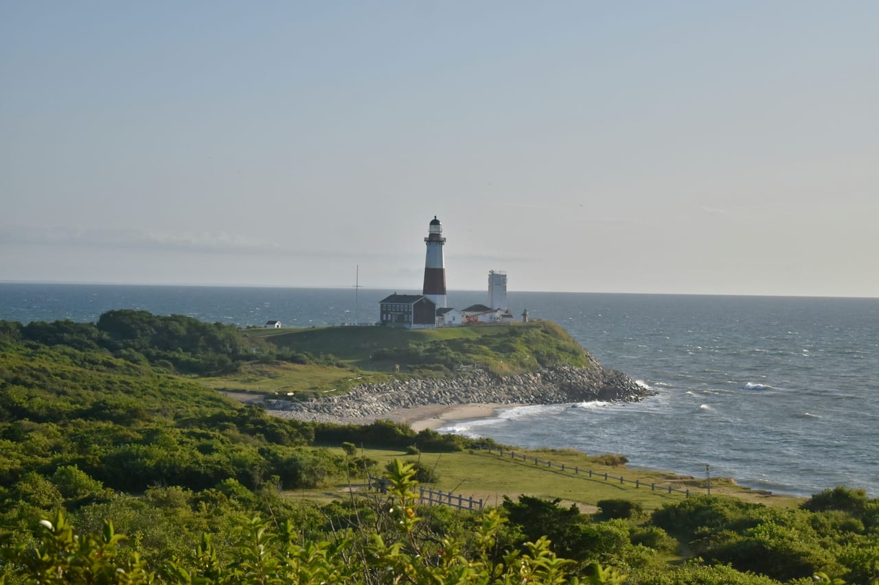 A lighthouse stands on a green coastal point beside the ocean.