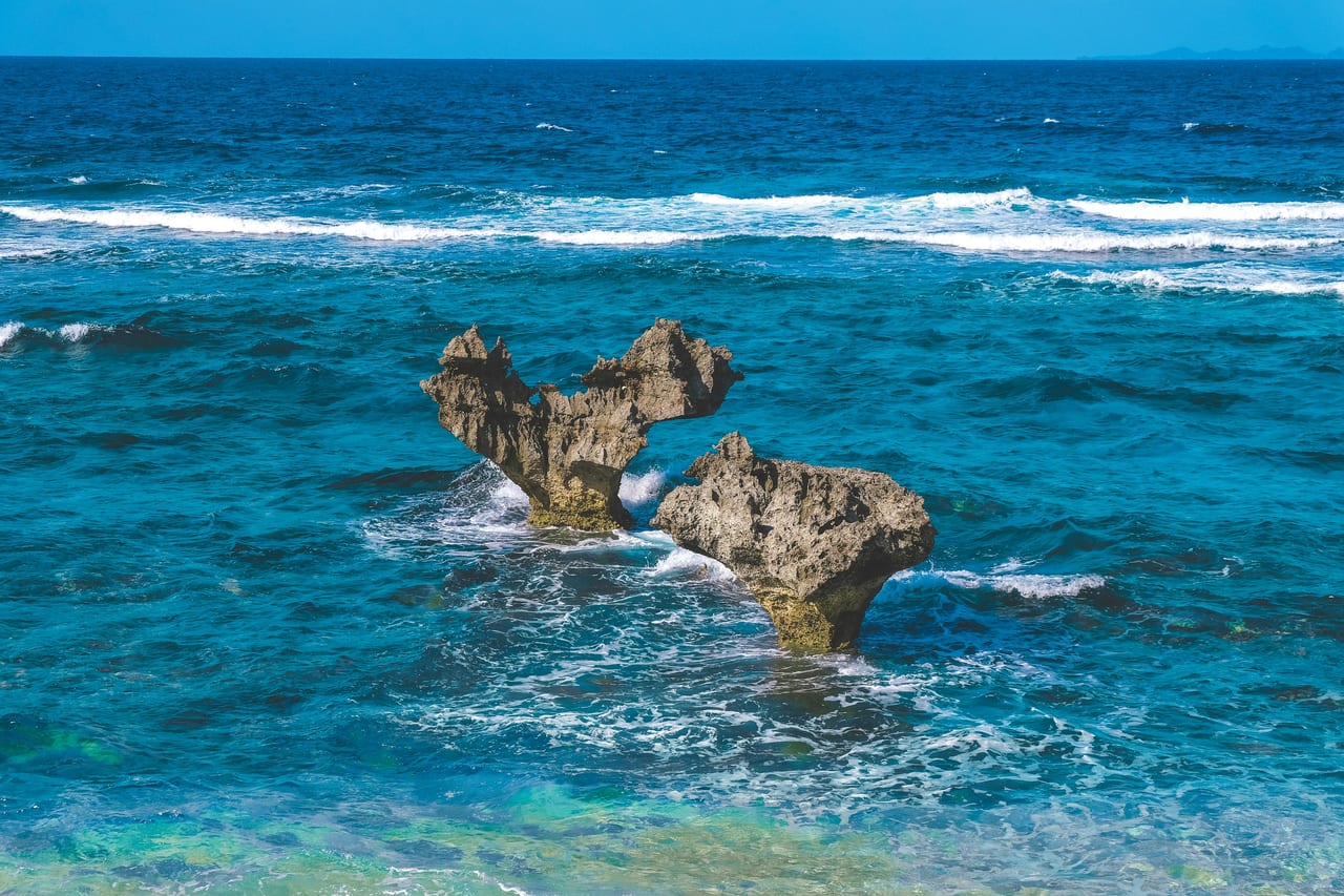 A distinctive rock formation sits in bright blue ocean water.