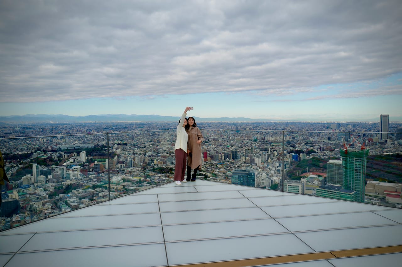 A visitor stands at the rooftop edge of Shibuya Sky as Tokyo's cityscape stretches to the horizon below.