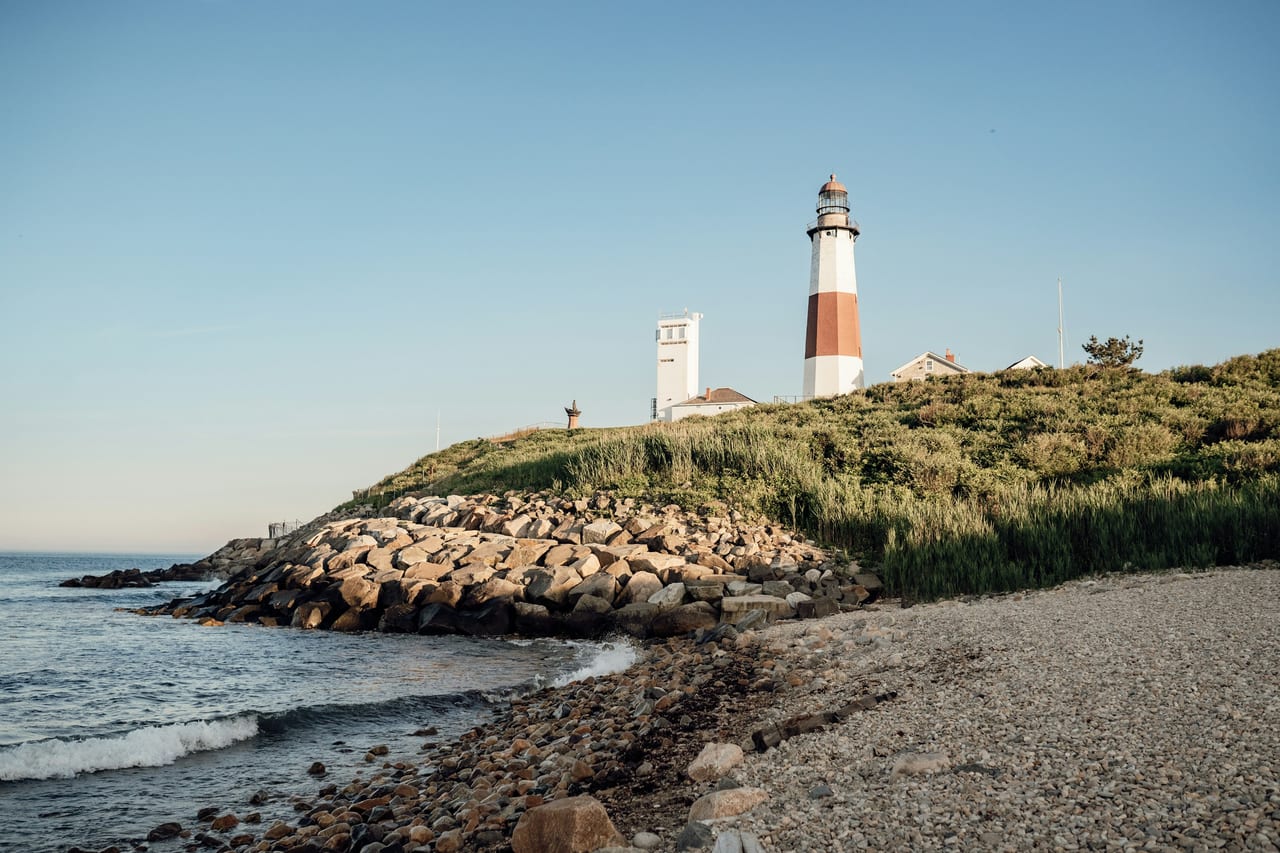 Montauk Point Lighthouse stands above a rocky shoreline and low coastal vegetation.