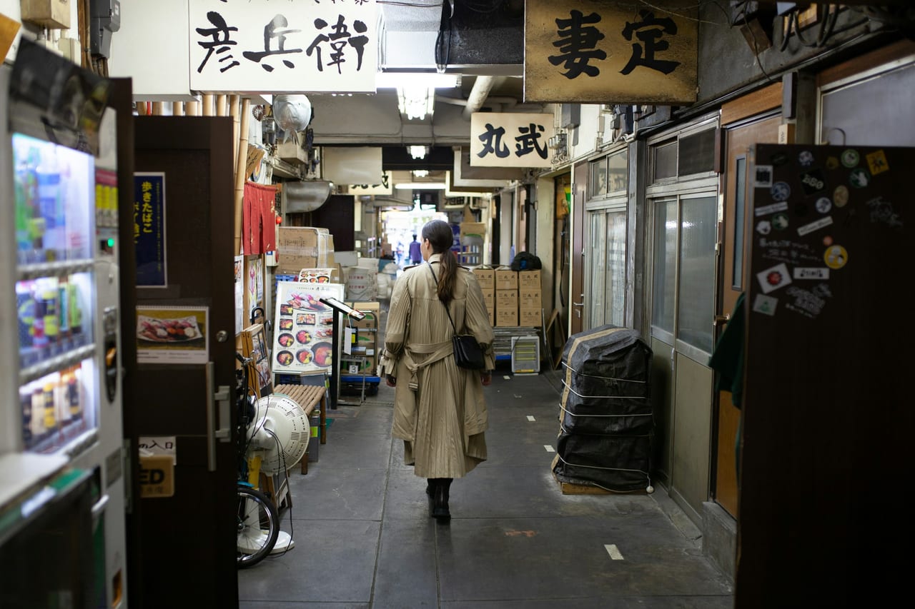 Shoppers pass the food stalls and shopfront signs of the Tsukiji outer market's covered alleys.