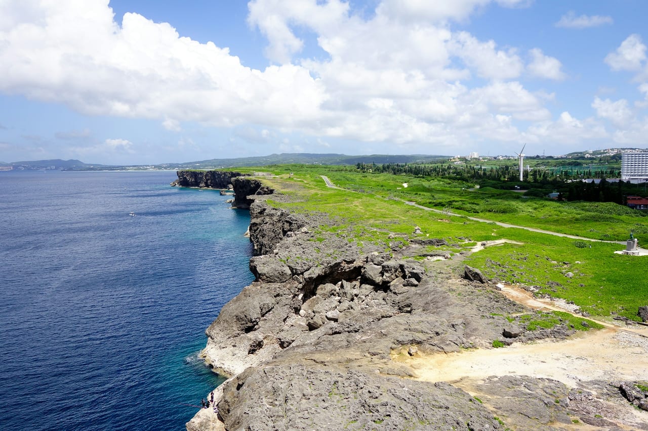 A grassy rocky coastline beside the sea under a bright blue sky.