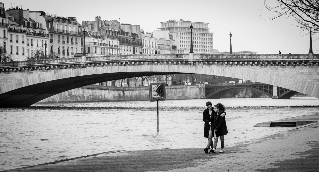 Couple walking across one of the Seine bridges in Paris, the river and Haussmann buildings in the background.