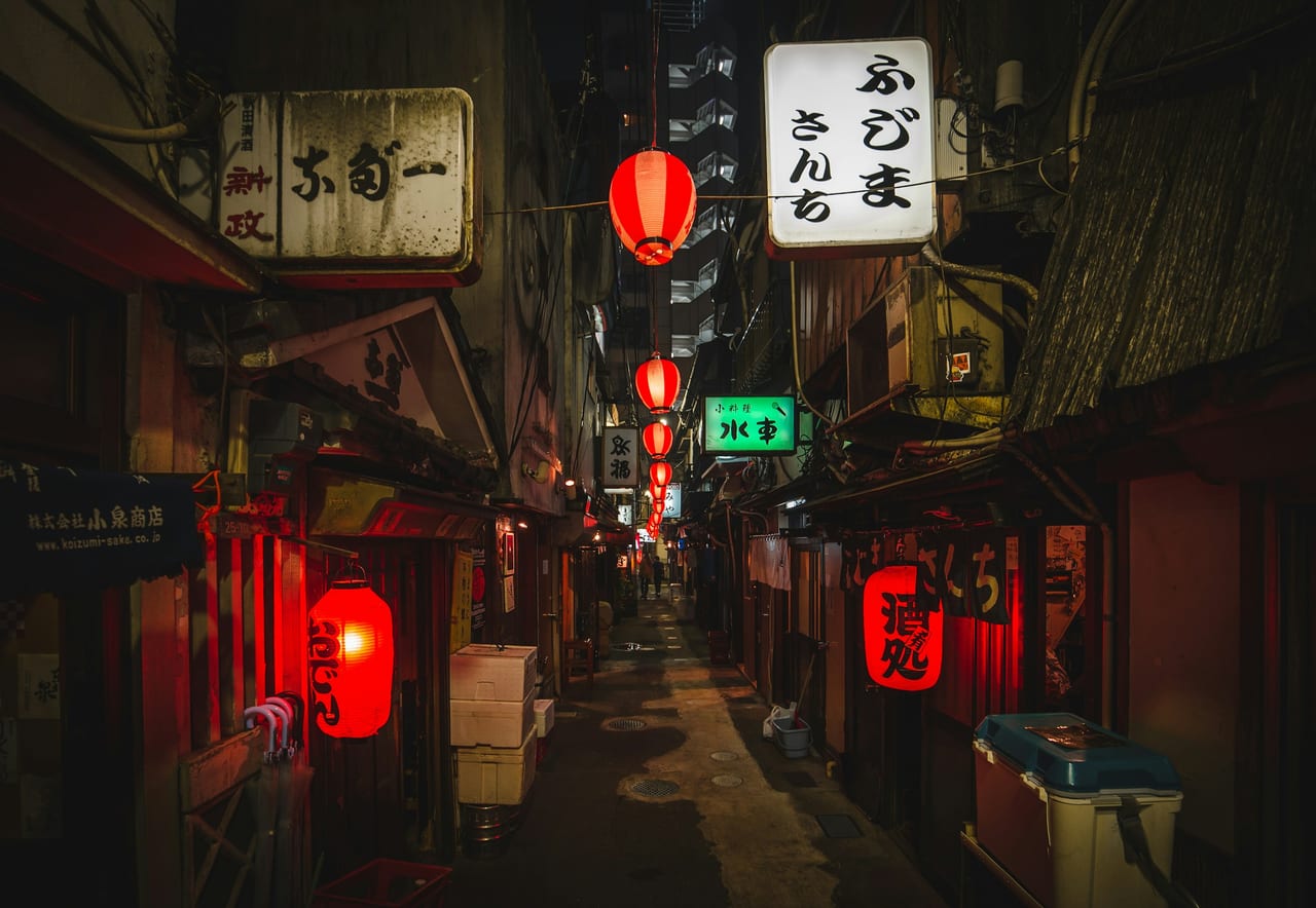 Red paper lanterns and glowing izakaya signs line a narrow Tokyo nightlife alley after dark.