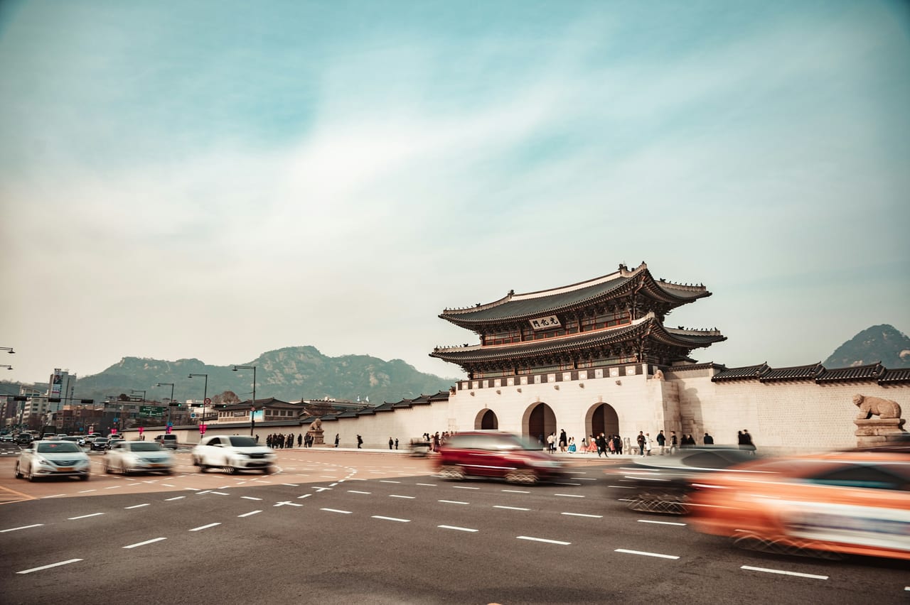 Gwanghwamun Gate stands beyond a busy roadway with mountains behind it in Seoul.