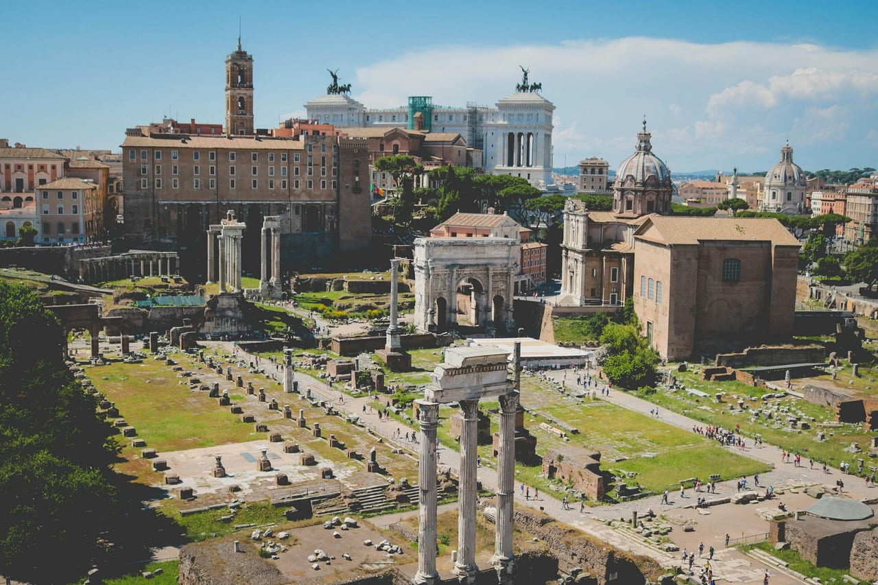 Broken temple columns and ruins of the Roman Forum stretch toward the hills of ancient Rome.
