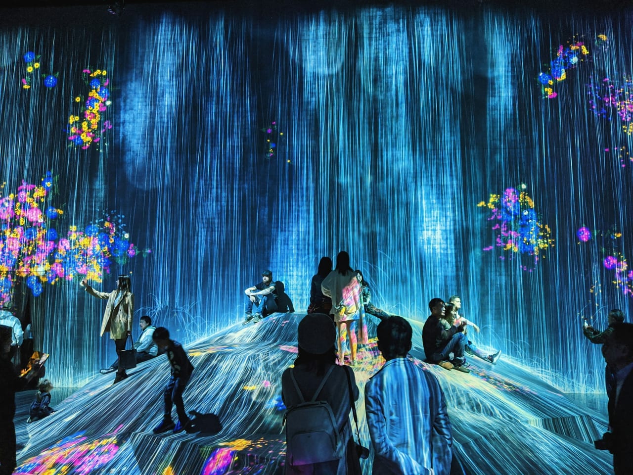Visitors wade through shin-deep water as projected koi and flowers ripple across the dark walls of teamLab Planets.