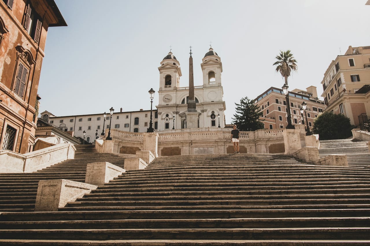 The empty Spanish Steps sweep up to the twin-towered church of Trinita dei Monti and its obelisk under a bright sky.