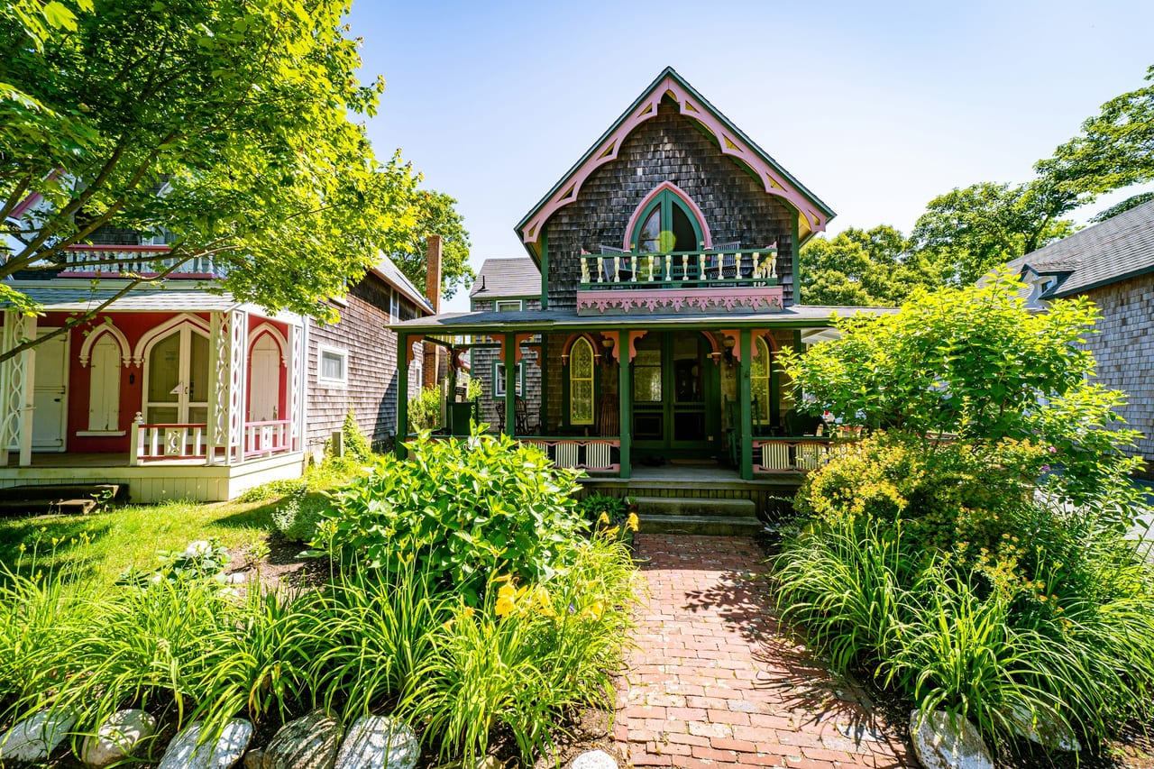 A dark-shingled cottage with a decorated gable stands among gardens.