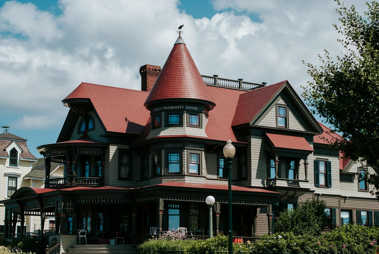 A large red-roofed Victorian building stands beneath a partly cloudy sky.