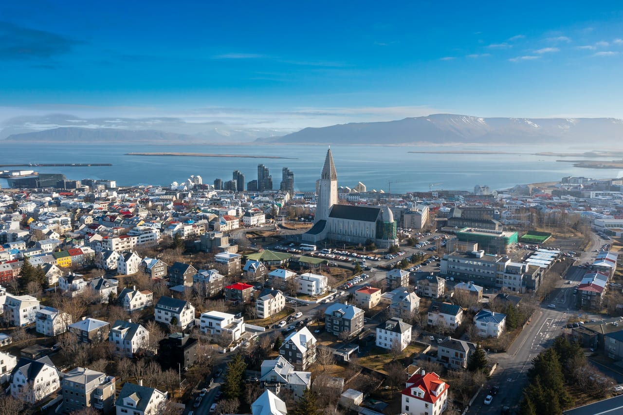 Aerial view of Reykjavik showing Hallgrimskirkja, colorful houses, the sea, and mountains.