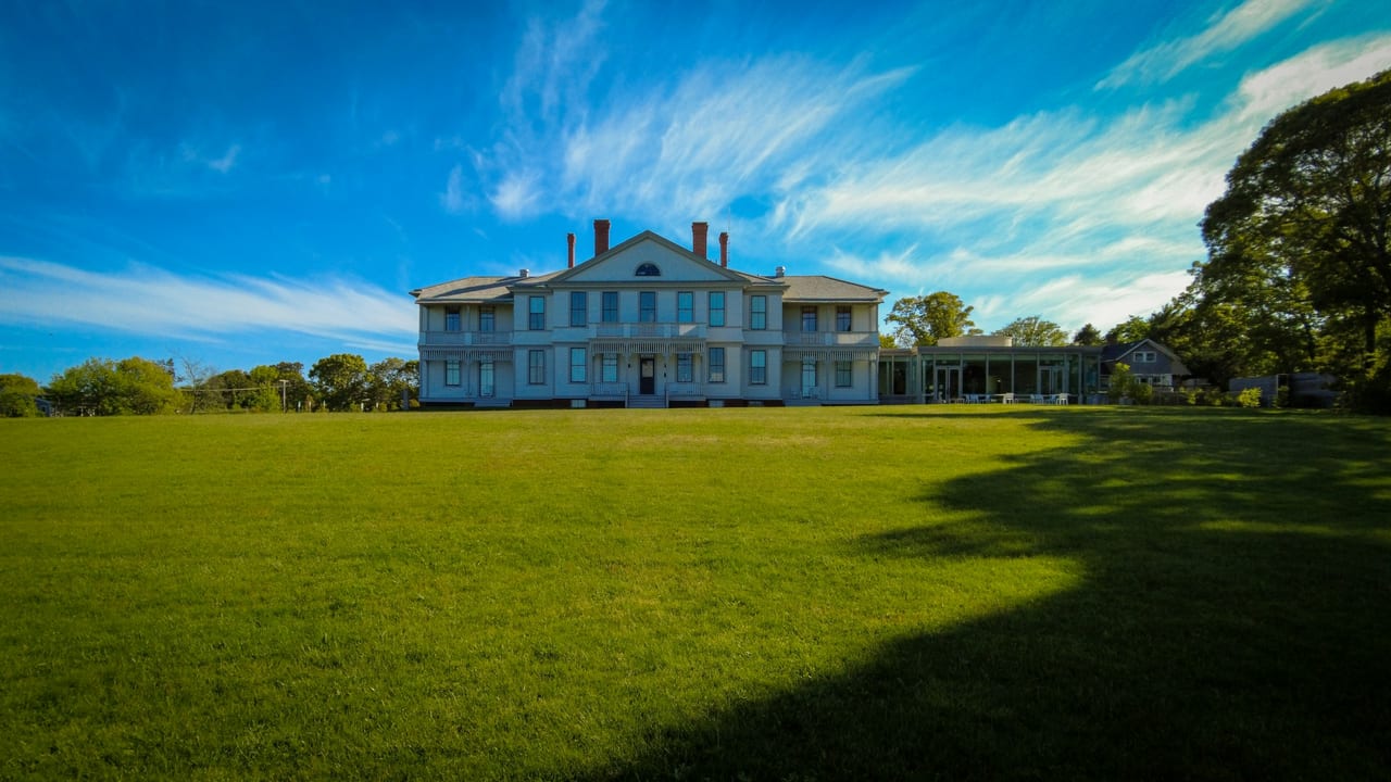 A large pale building stands at the far side of a broad green lawn beneath a blue sky.