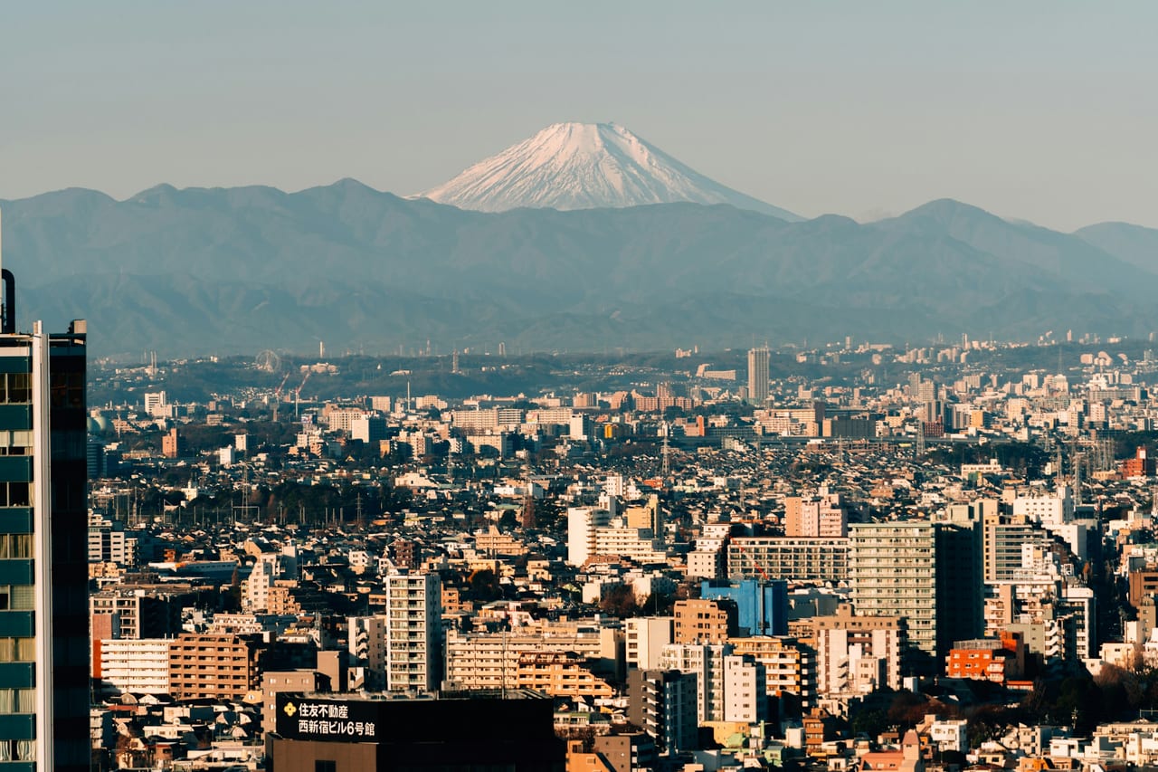 A snow-capped Mount Fuji rises in clear daylight beyond Tokyo's vast cityscape.