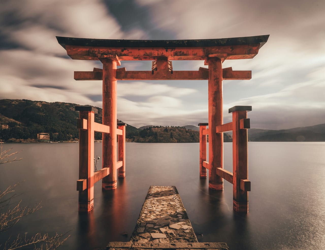 The vermilion Heiwa-no-Torii of Hakone Shrine stands in the still water of Lake Ashi at the end of a stone jetty.