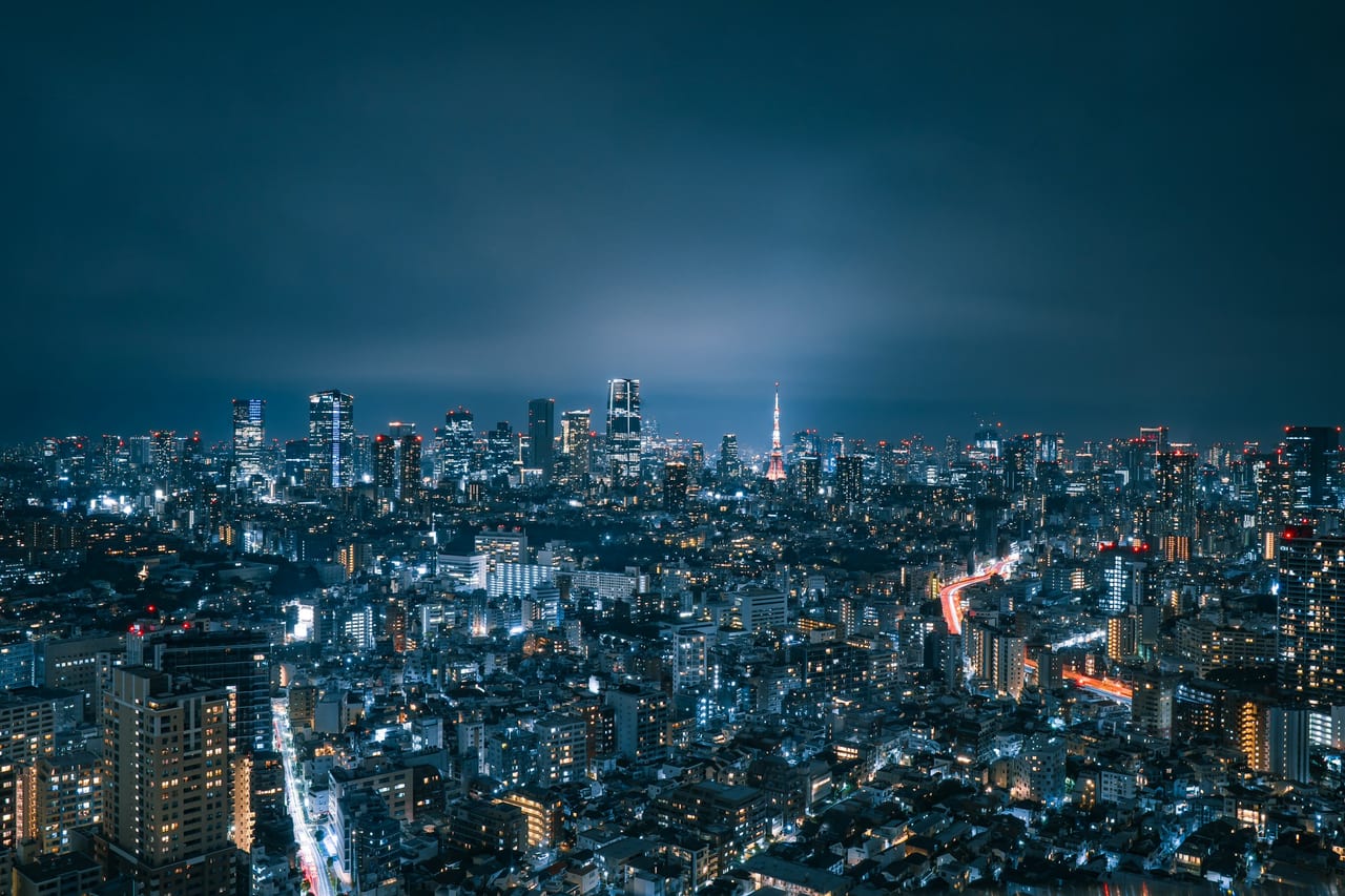 Tokyo's illuminated cityscape sprawls to the horizon at night, the distant Tokyo Tower glowing amid a sea of lights.