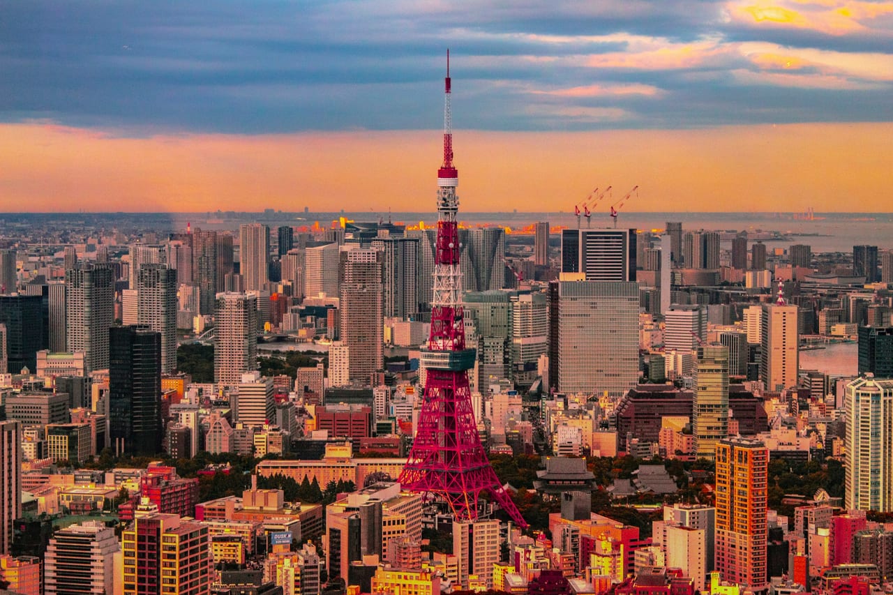 Tokyo Tower glows red and white above the dense city skyline under a golden sunset.