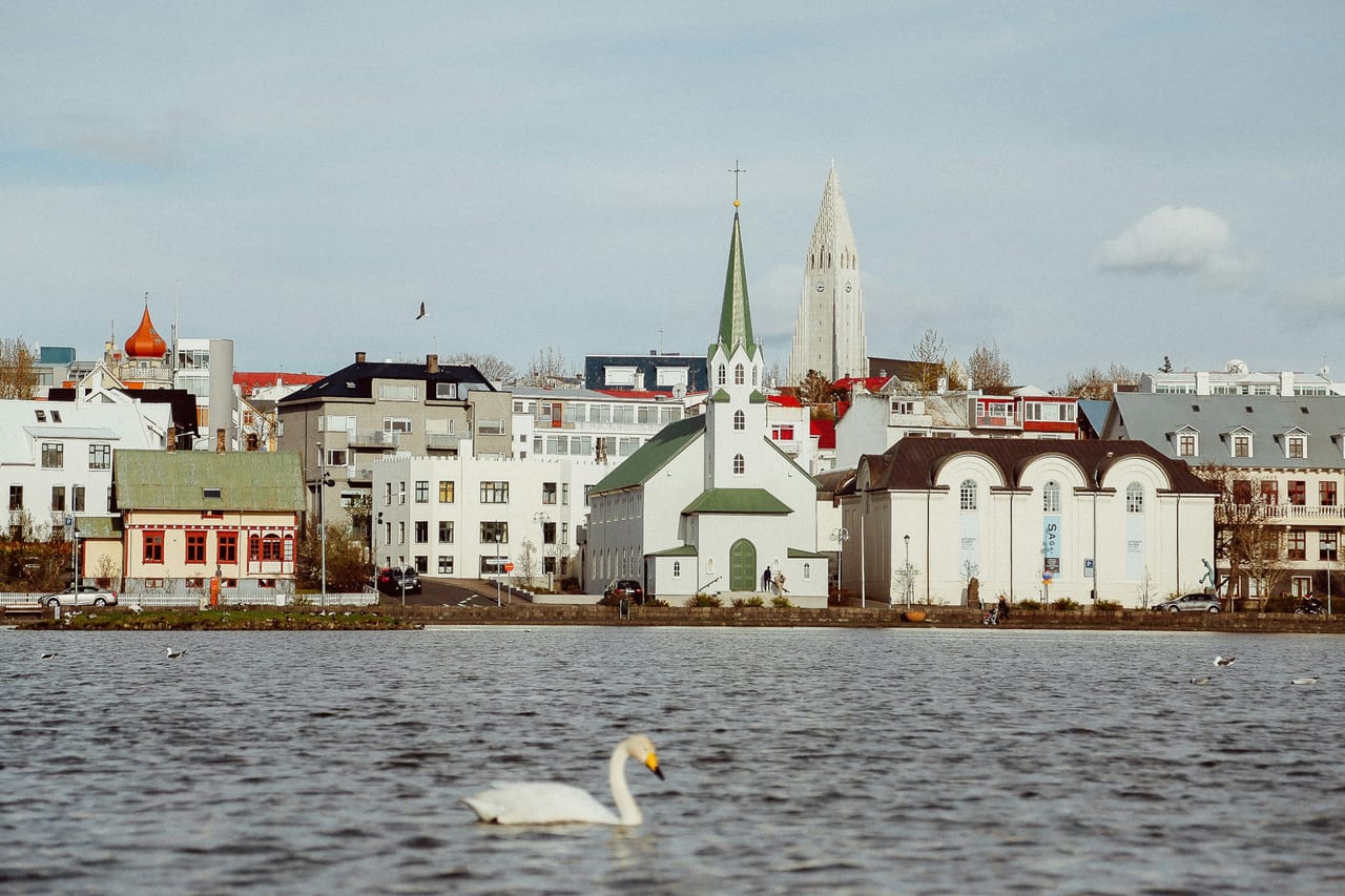 A waterfront view of central Reykjavik with colorful buildings and church spires beyond the water.
