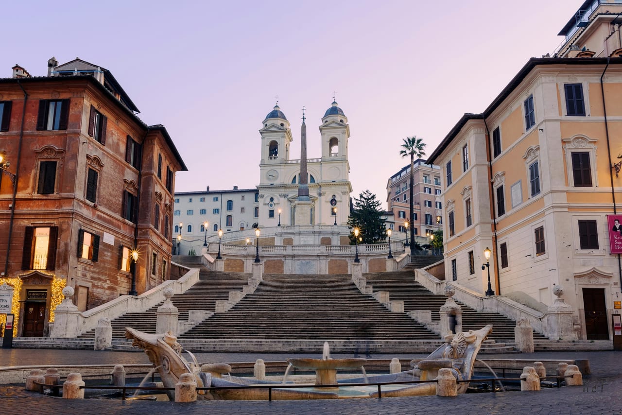 The Barcaccia fountain sits at the foot of the Spanish Steps, which climb to the twin-towered Trinita dei Monti at dawn.