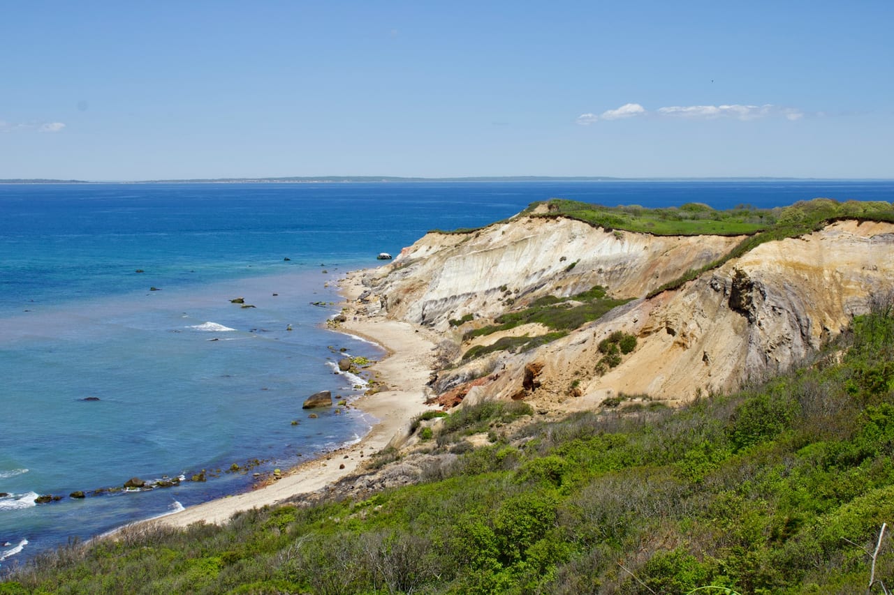 White coastal cliffs curve along a blue ocean beneath a clear sky.