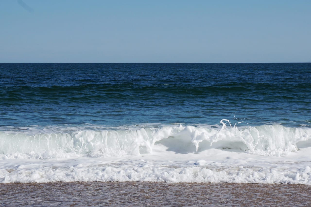 Waves break along a sandy beach beneath a clear blue sky.