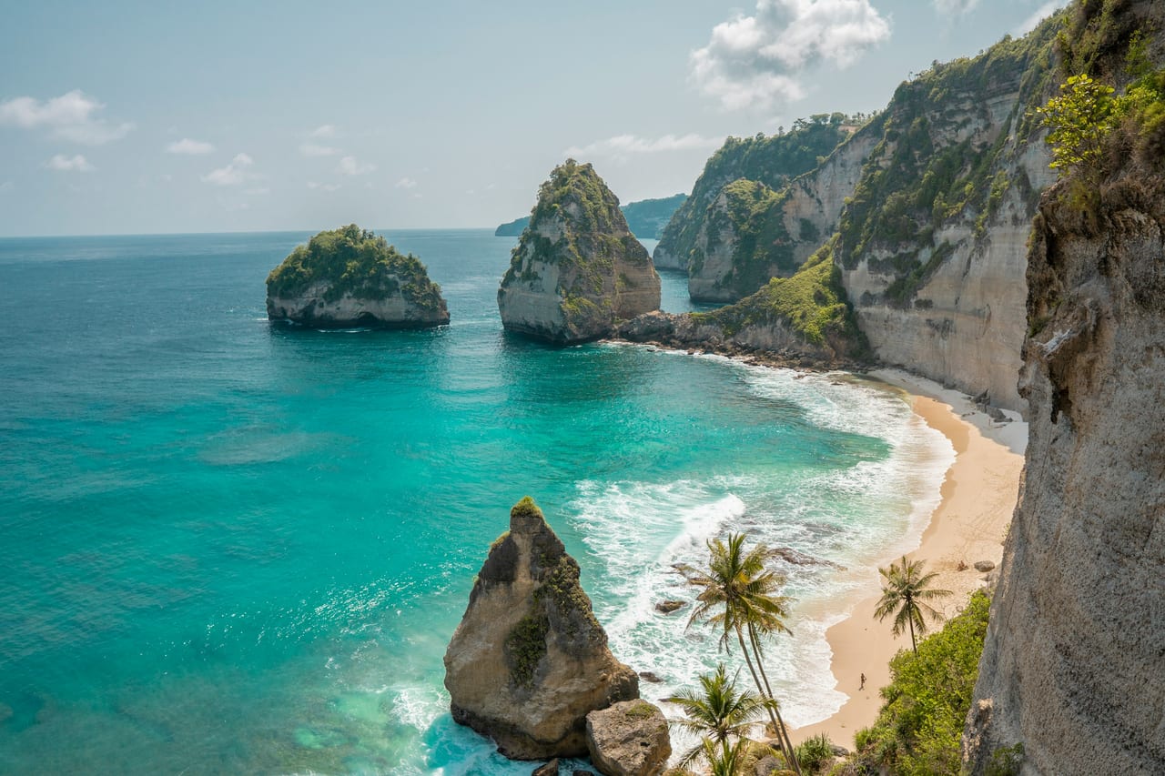 A turquoise bay with steep green limestone cliffs, rock islets, and a sandy beach.