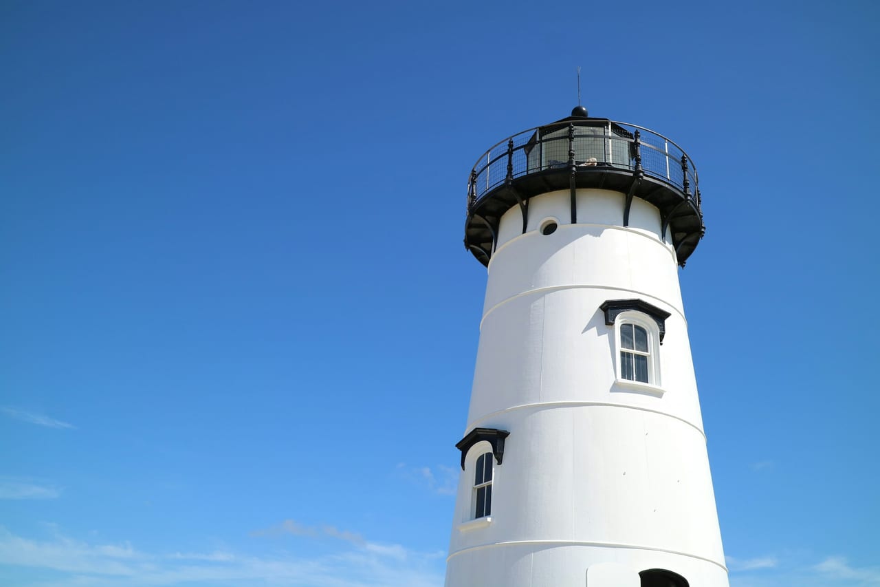 A white lighthouse rises against a clear blue sky.