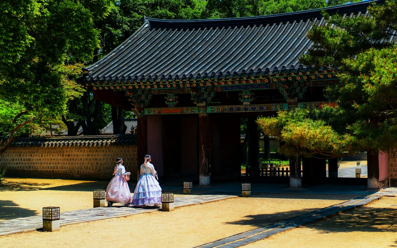 A traditional Korean gate with two people in hanbok in a palace courtyard in Seoul.