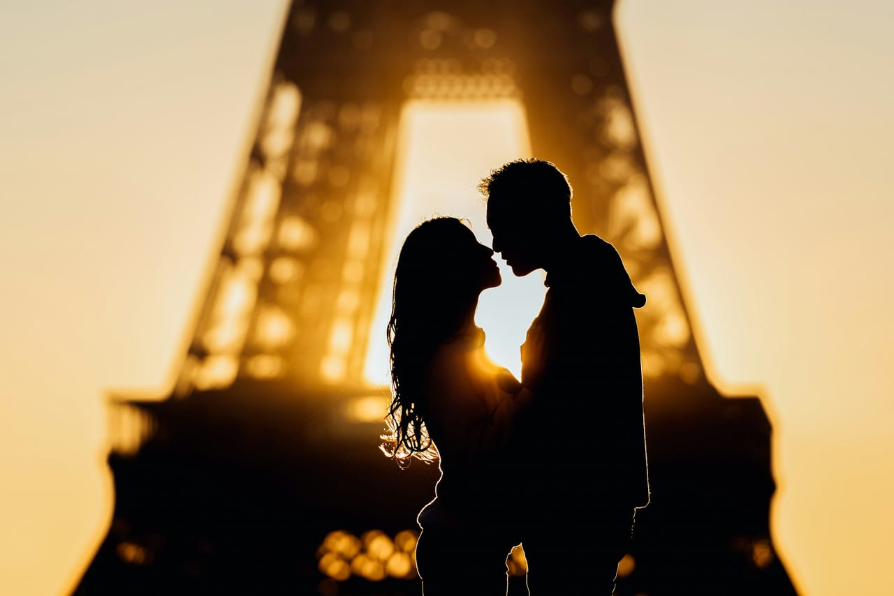 Couple watching sunset over the Paris skyline with the Eiffel Tower in golden evening light.