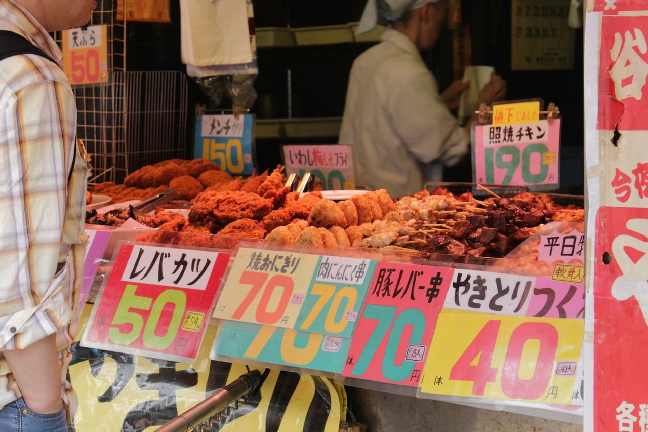 A Tsukiji outer market stall is lined with trays of cooked food and bright yellow price signs.