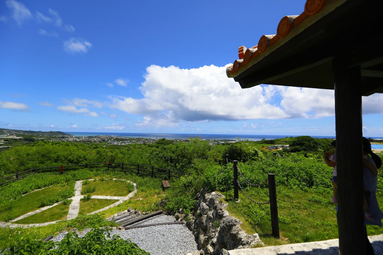 A stone path crosses green grounds beside a traditional tiled roof, with the sea beyond.