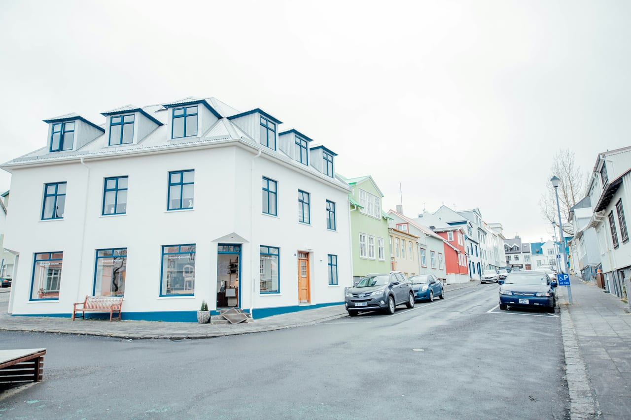 A white corner building stands on a Reykjavik street lined with colorful houses and parked cars.