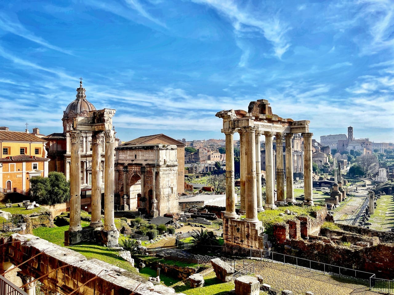 Ruined temple columns and the Arch of Septimius Severus stand across the Roman Forum on a clear day.