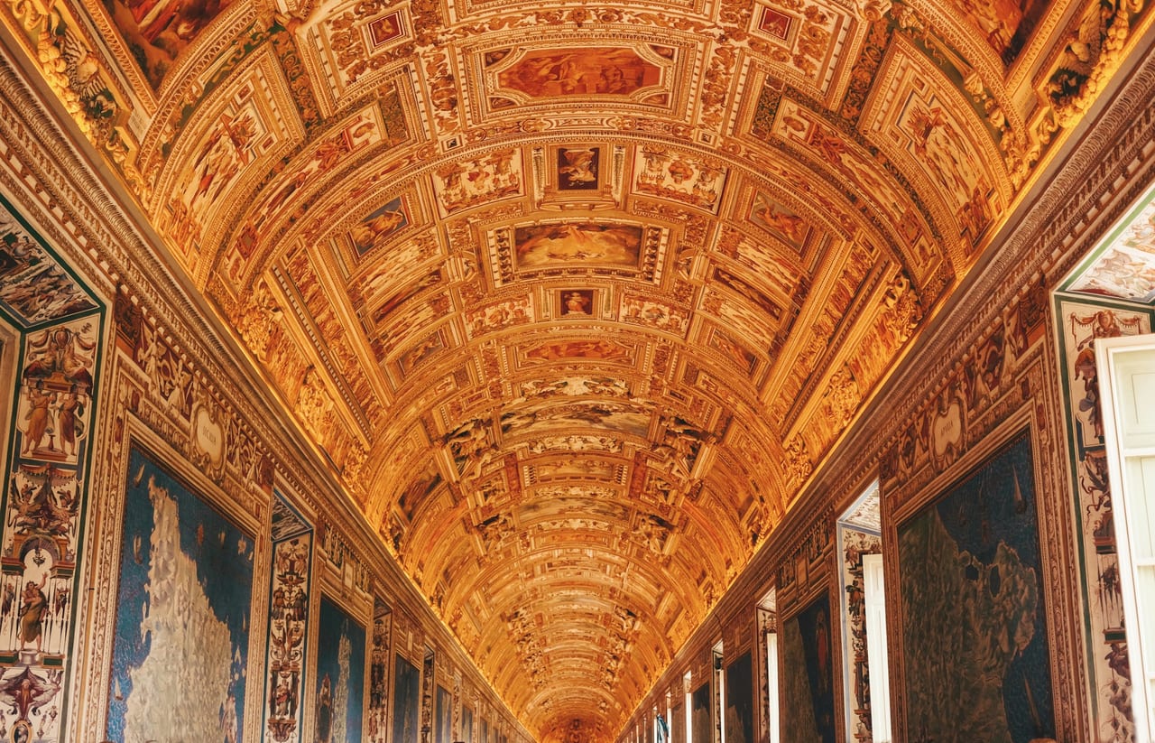 The gilded, fresco-vaulted ceiling of the Vatican Museums' Gallery of Maps recedes down the corridor.
