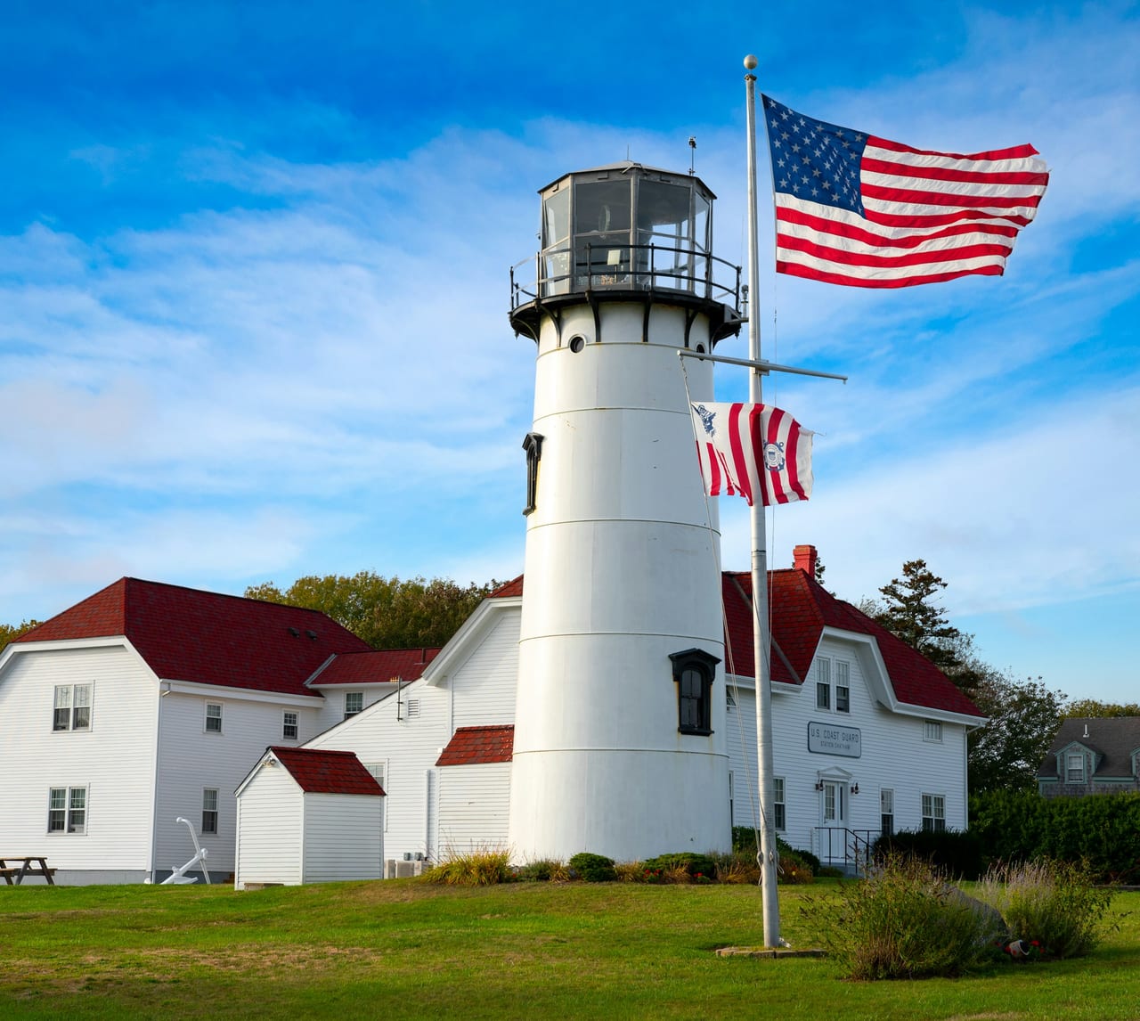 White and red concrete lighthouse near a white and red house under blue sky during daytime