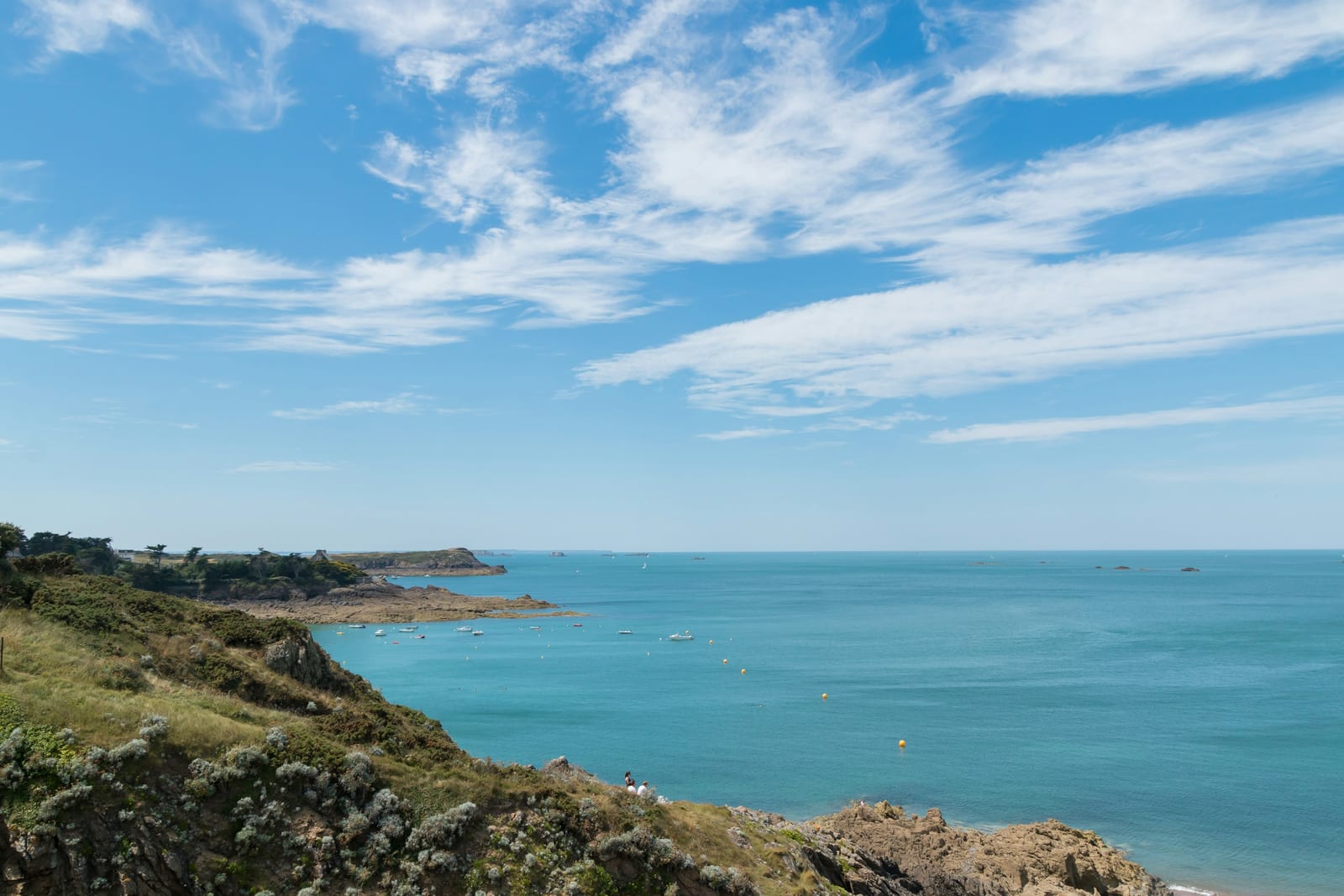 A rocky coastline borders a bright blue ocean beneath a partly cloudy sky.