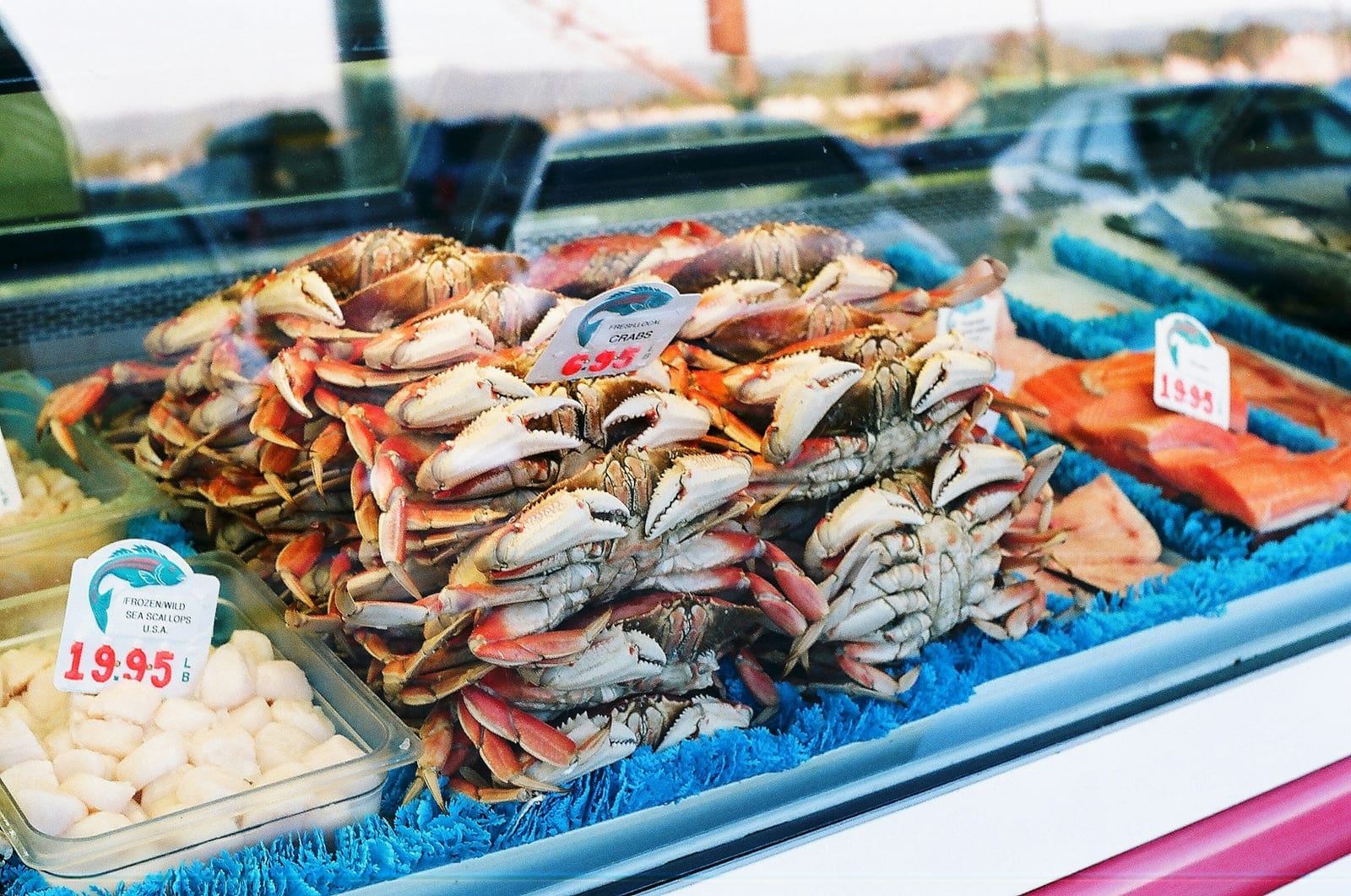 A brightly lit seafood counter displays piles of crab, shrimp, and other shellfish on ice.
