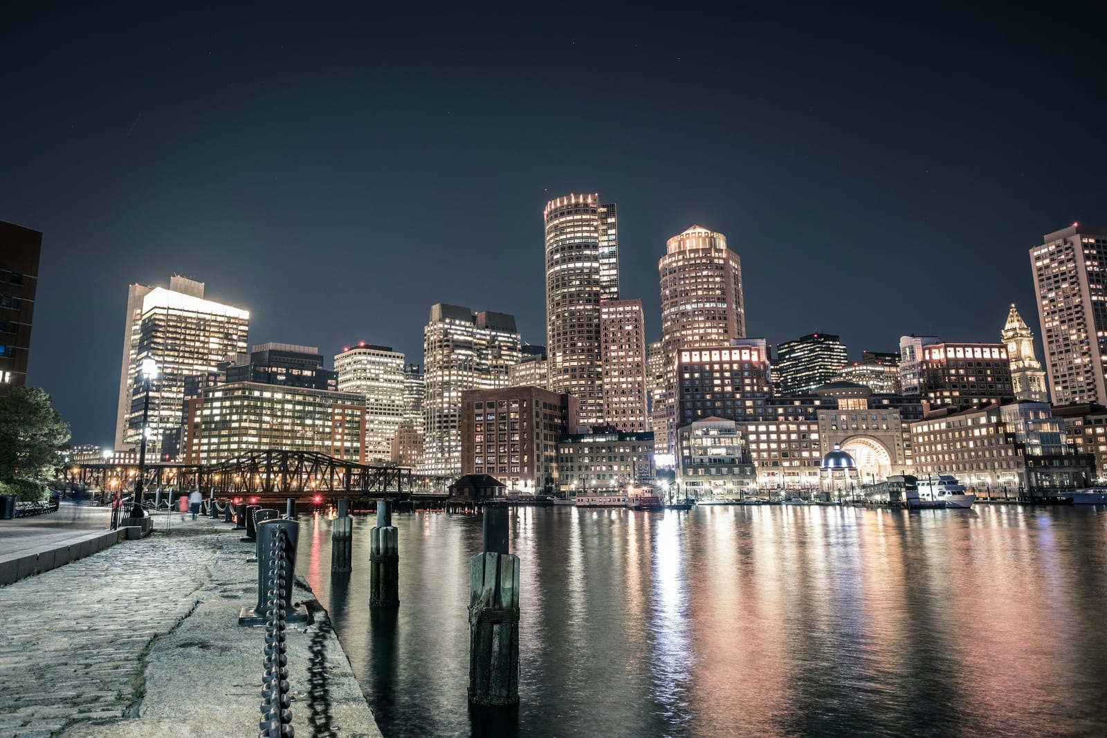 The Boston waterfront with modern buildings and a pedestrian walkway along the harbor.