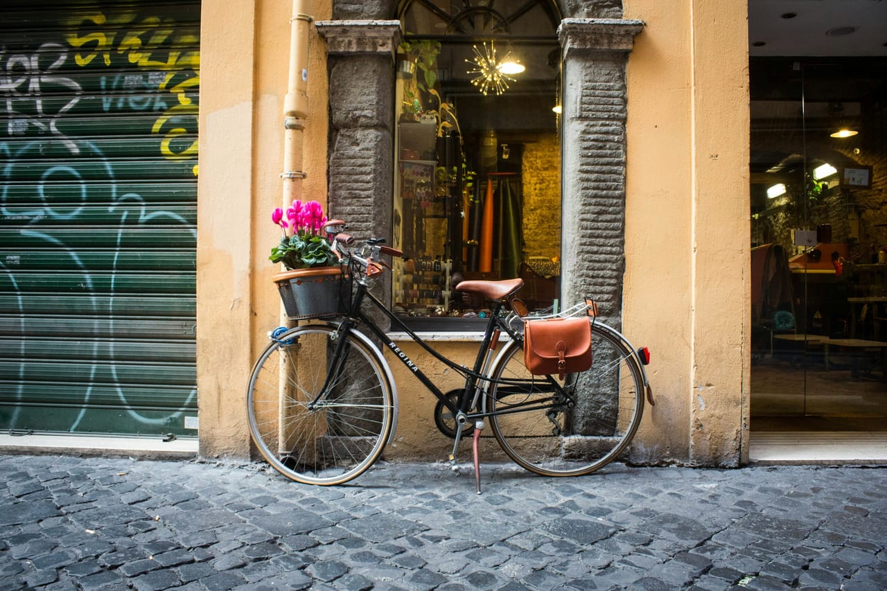 A red bicycle loaded with produce baskets leans by the laden stalls of a Rome food market.