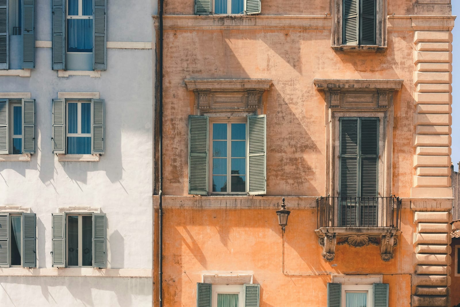A warm ochre facade with green shutters on a quiet street in the Monti rione, Rome.