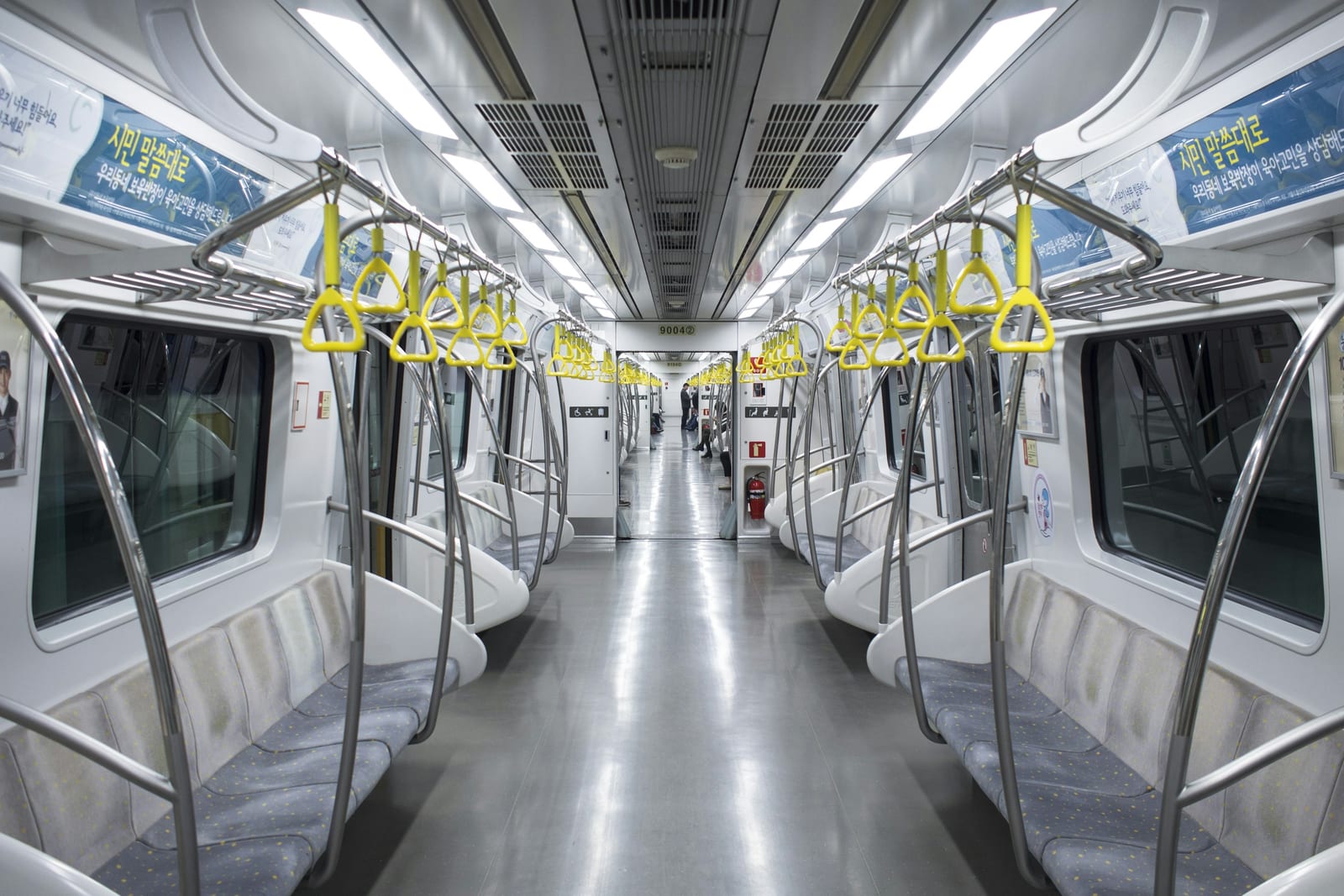 Bright, empty Seoul subway car with rows of seats and yellow hand straps.