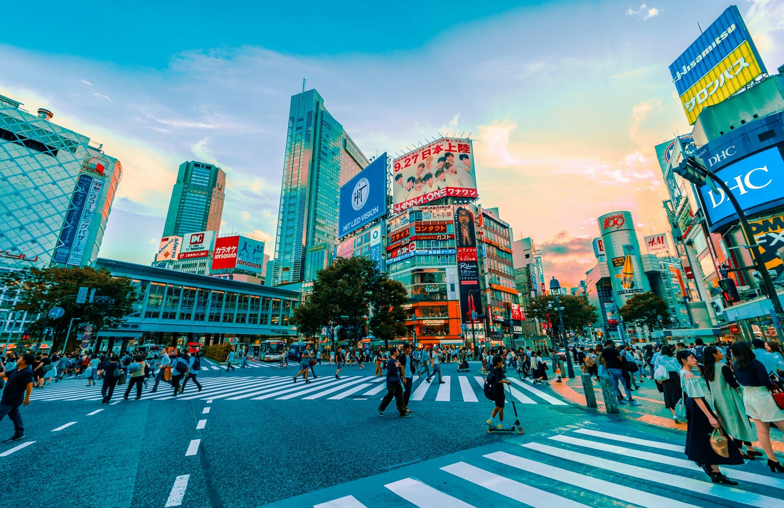 Crowds streaming across the Shibuya Scramble under neon signs.