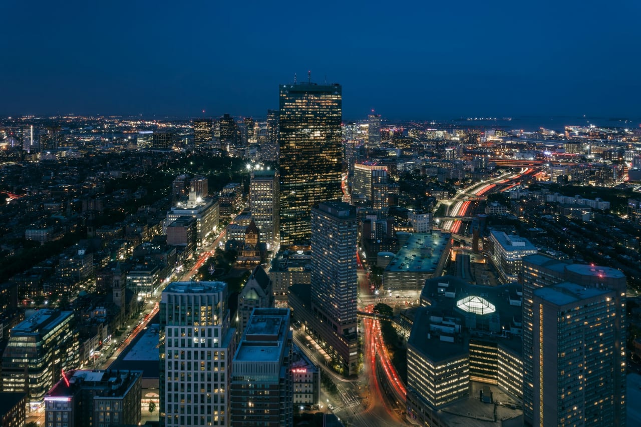 The Boston skyline and Charles River seen from above at dusk, with the Prudential Tower in the foreground.