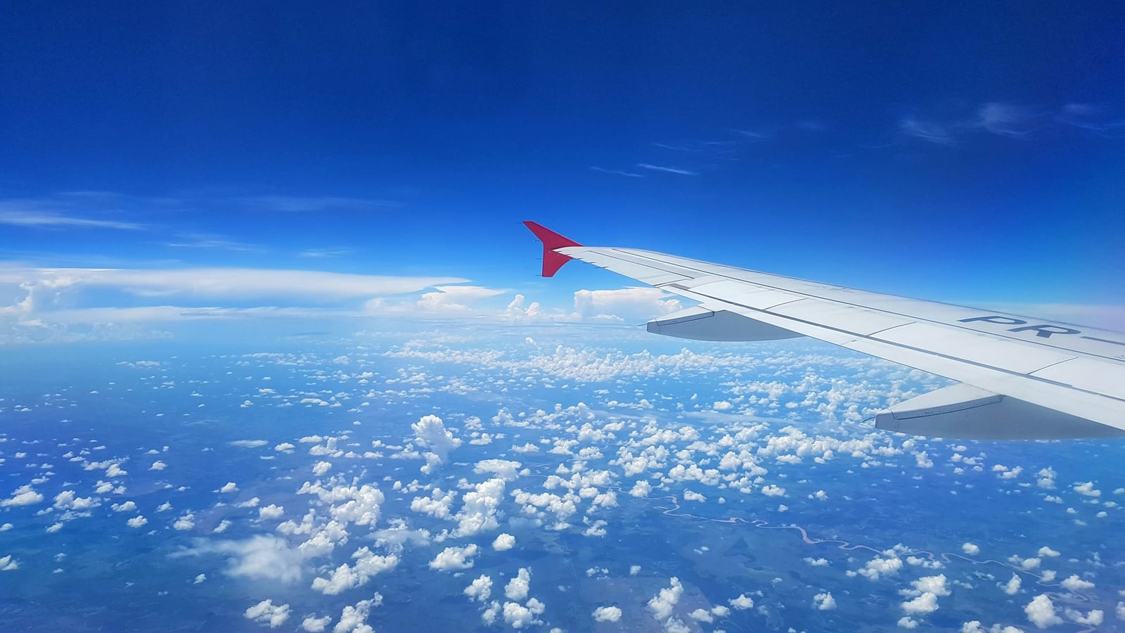 An airplane wing stretches over scattered white clouds beneath a clear blue sky.