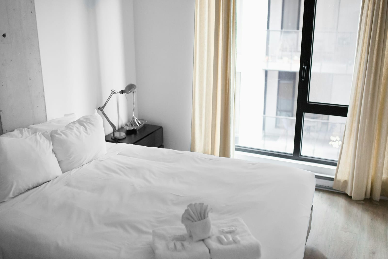 A bright, simple hotel room in Rome with a crisply made white bed and a large window letting in daylight.