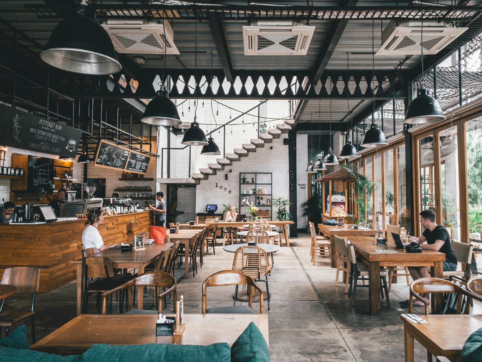 A busy indoor food hall with communal tables and diners under warm pendant lights.