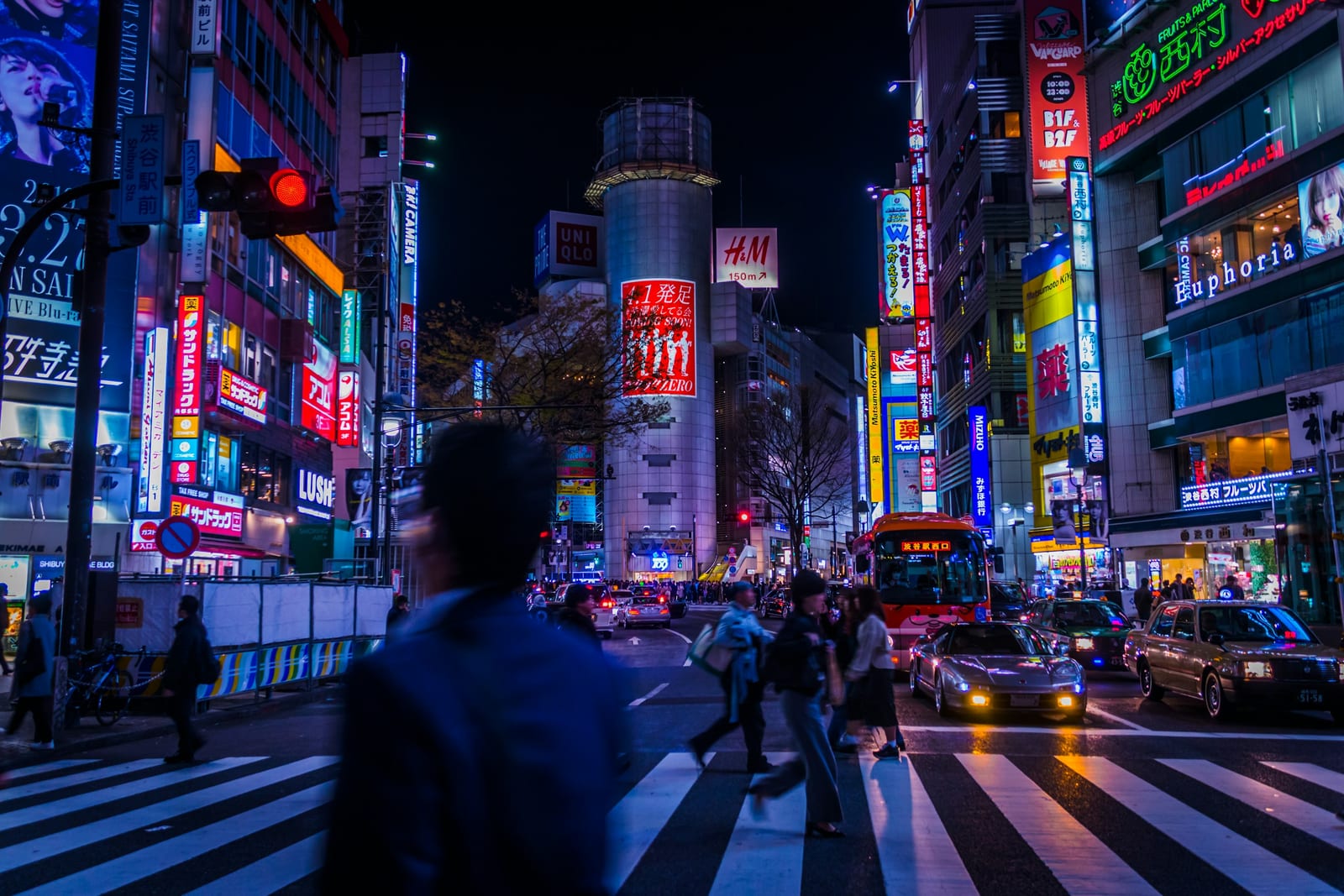 Crowds streaming across the Shibuya Scramble under neon signs.